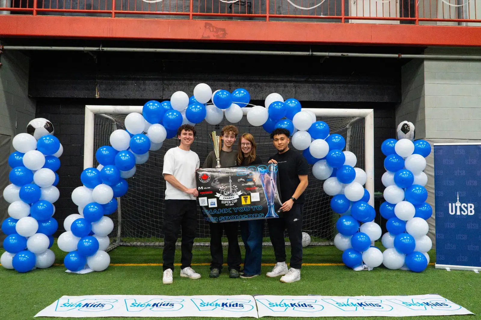 Charity Super Cup organizers presenting the tournament trophy in front of a SickKids banner